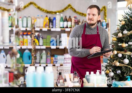 Bearded man seller restock of goods using tablet in store decorated for New Year holiday Stock Photo
