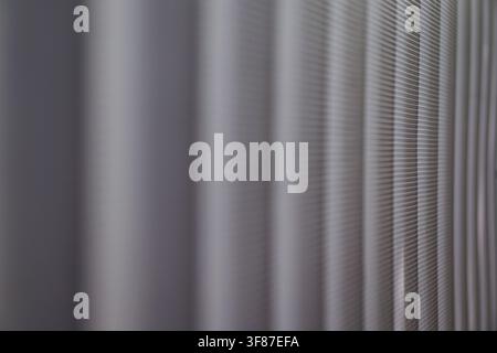 Minimalist close-up of a grey perforated metal surface featuring rhythmic vertical folds and shallow depth of field. Stock Photo
