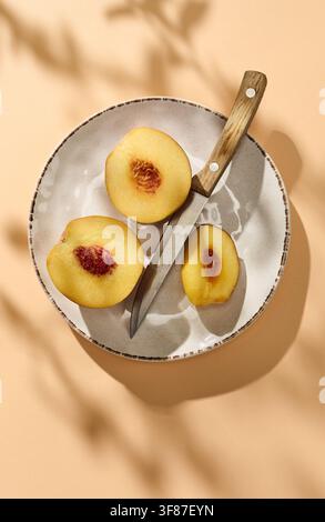 plate of Fresh juicy sliced peach and knife arranged on a soft pastel colored background, photographed from above in warm natural sunlight. Bright sum Stock Photo