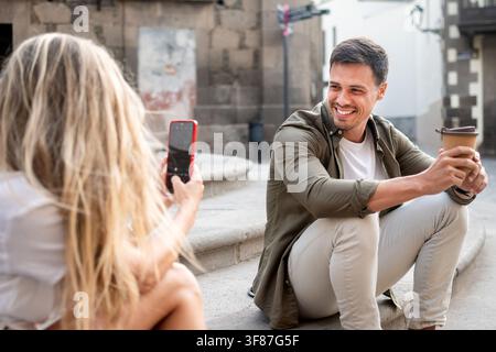 Woman photographs her smiling boyfriend holding a takeaway coffee. Stock Photo