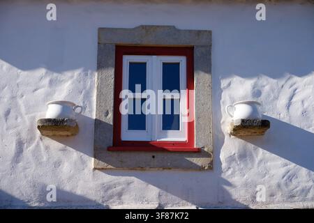 Traditional portuguese white wall with a red window frame and decorative ceramic pots Stock Photo