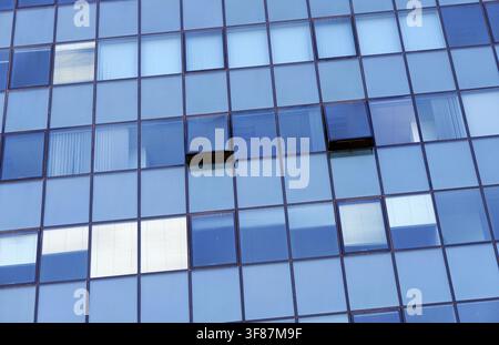 Modern skyscraper exterior featuring a blue glass facade forming a grid pattern, with several windows open for ventilation, creating a dynamic archite Stock Photo