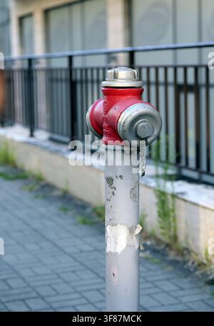 Red fire hydrant standing on a paved sidewalk in an urban setting, representing crucial infrastructure for emergency services and public safety, ensur Stock Photo