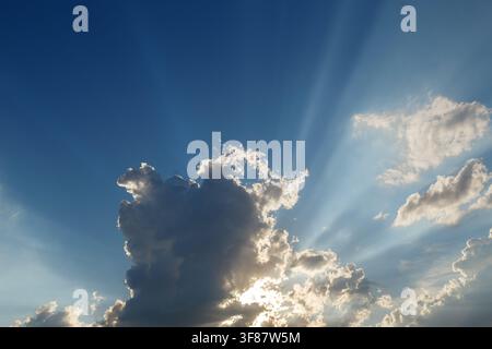 Dramatic blue sky with sun rays shining through fluffy white clouds Stock Photo