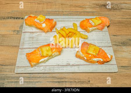 Four Salmon and Brie Toasts Arranged Around French Fries on Whitewashed Board Stock Photo