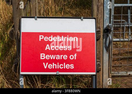 Red sign warning "Pedestrian Access Beware of Vehicles" on a field gate informing people to watch out for vehicles Stock Photo