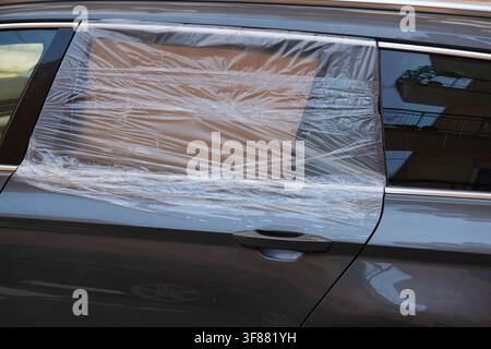 Broken car window covered with temporary plastic foil after car break-in. Crime concept in Bari, Italy. Stock Photo