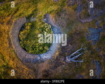 Aerial view of the circular stone ruins in the Anggard Mountains, surrounded by lush green vegetation, golden grasses, and a fallen dead tree in Gothe Stock Photo