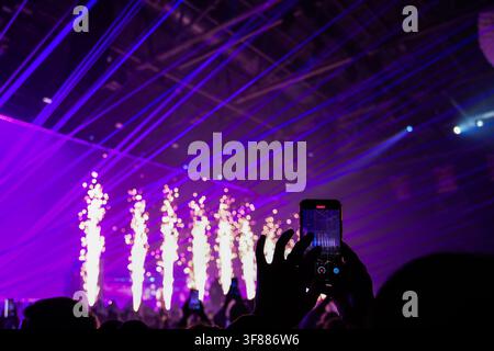 Ryazan, Russia, 28.09.2025 Woman hand holding smartphone recording concert with bright laser light beams and pyrotechnic effect. Night event. Stock Photo