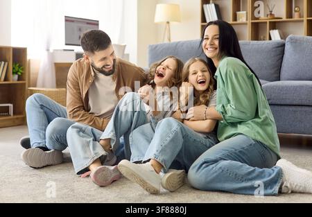 Happy parents tickling two sisters on living room floor, playful family bonding Stock Photo