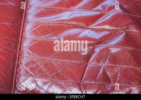 Detailed macro perspective showing aged, cracked red leather upholstery material with stitched seam line on oldtimer vintage classic vehicle driver se Stock Photo