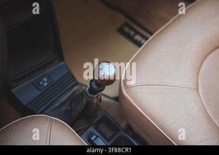 High angle interior shot showing wooden 5-speed manual gear shift lever, center console, and beige leather bucket seats inside a classic Saab car. Stock Photo
