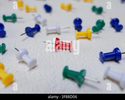 Colorful push pins are scattered over textured white board, red push pin as focus. Stock Photo