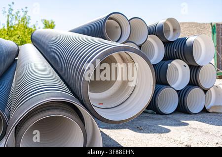 corrugated pipes neatly stacked on a concrete surface in an outdoor construction site, viewed from a ground-level perspective, highlighting industrial Stock Photo