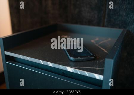 Modern smartphone lying on dark marble bedside table top Stock Photo
