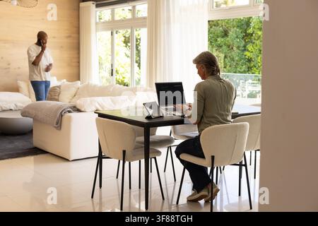 Couple with senior woman using laptop and tablet at dining table while man speaking on smartphone. Home, openplan, modern, minimalist, windows, light, Stock Photo