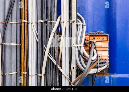 Industrial electrical cables and wires bundled together on metal brackets next to orange junction box against blue wall background Stock Photo
