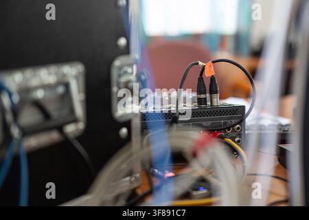 Audio cables with XLR and RCA connectors are plugged into the rear panel of a sound mixer console next to a flight case in a studio setup. Stock Photo