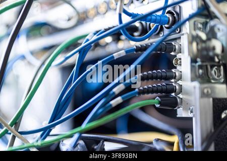 A detailed close-up of blue and green SDI and audio cables connected into the rear patch panel of a broadcast server rack in a professional production Stock Photo