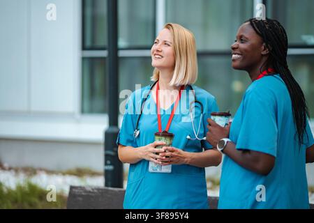 Diverse female medical workers smiling having coffee break outdoors Stock Photo