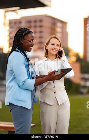 Businesswomen collaborating outdoors using digital tablet and smartphone Stock Photo