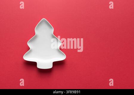 Christmas concept with empty white plate shaped as Xmas tree on red background. Xmas greeting card. View from above. Copy space Stock Photo