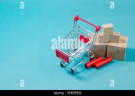 Small metal shopping cart positioned near stacked wooden blocks on a blue surface for retail, supply chain, and commerce topics. High Quality Photo Stock Photo