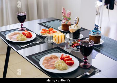 Easter festive table setting with traditional food, cupcakes and red wine at home. Stock Photo