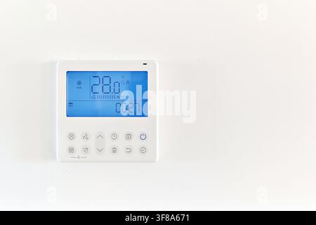 Digital thermostat control panel mounted on wall displaying twenty eight degrees Celsius temperature. Home climate control, temperature adjustment Stock Photo