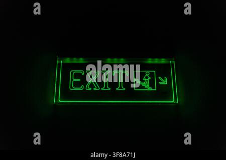 Bright green exit sign glowing in darkness, highlighting emergency stairs for safe evacuation and wayfinding in buildings. Stock Photo
