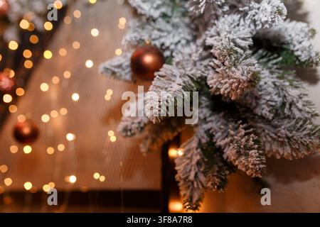 Soft focused shot of snowy fir-tree branches decorated with golden baubles and shiny garland lights bokeh on blurry background, copy space. Winter hol Stock Photo