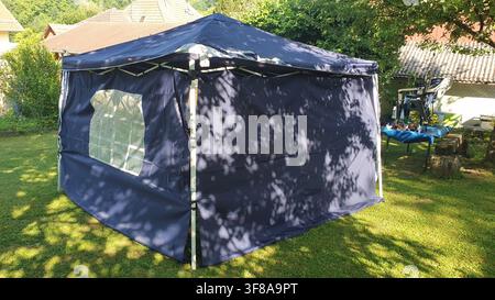 A navy blue popup gazebo stands on green grass in a sunny backyard Stock Photo