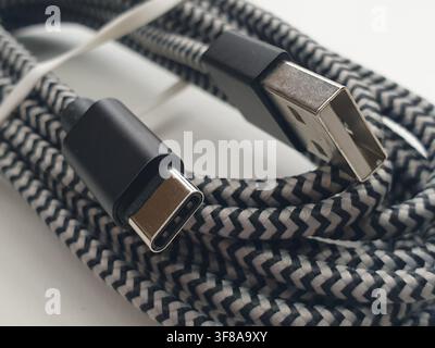A black and white braided USB cable lies on a white surface Stock Photo
