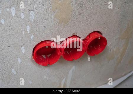 Red electrical junction boxes recessed into a gray concrete wall during renovation, ready for wiring and outlets as part of residential construction a Stock Photo