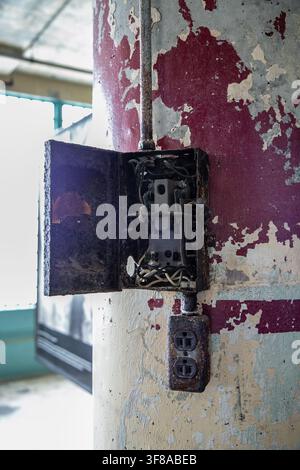 Abandoned wall-mounted industrial electrical control panel with heavily rusted metal cabinets, open hinged doors, and exposed vintage electrical parts Stock Photo