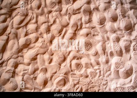 Close-up of overlapping footwear tread impressions pressed into a sandy ground surface, showing variety of distinct sole patterns from multiple shoes Stock Photo