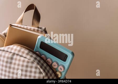 Checkered school backpack with notebook and blue calculator in warm light Stock Photo