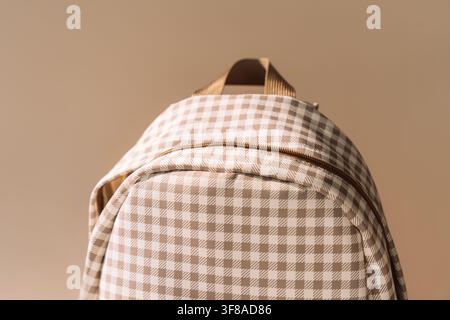 Beige checkered school backpack in warm sunlight, minimal back to school background Stock Photo