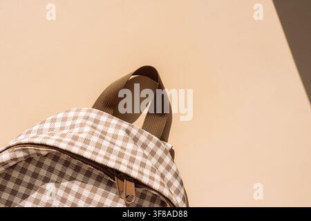 Beige checkered school backpack in warm sunlight with copy space, back to school concept Stock Photo