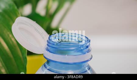 Macro view of open attached cap on blue plastic water bottle near green plant leaves eco friendly design EU tethered cap directive concept stock photo Stock Photo