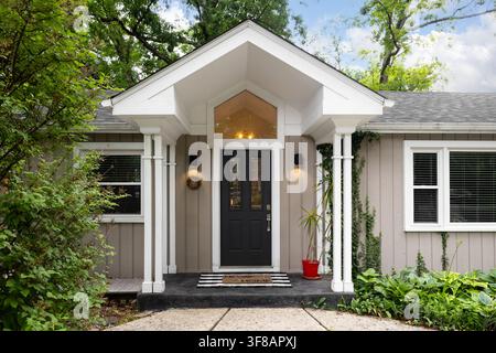 A black front door detail with glass windows under a tall white awning supported by white posts, brown vertical siding, and white trim. Stock Photo