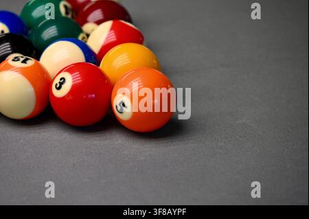 photograph of a complete rack of colorful numbered billiard and pool balls arranged in a classic triangle formation on a neutral gray background. Stock Photo