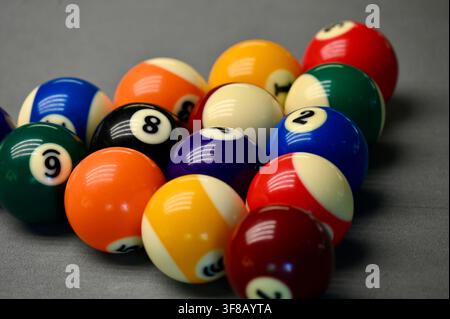 photograph of a complete rack of colorful numbered billiard and pool balls arranged in a classic triangle formation on a neutral gray background. Stock Photo