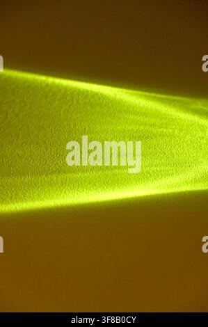 Commercial close-up photograph of an abstract bright yellow light beam or caustic reflection creating a sharp geometric shape on a dark, warm background. Stock Photo