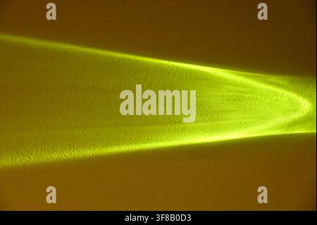 Commercial close-up photograph of an abstract bright yellow light beam or caustic reflection creating a sharp geometric shape on a dark, warm background. Stock Photo
