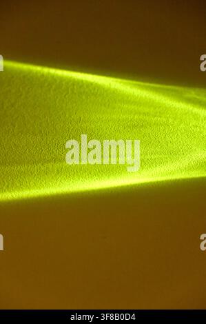 Commercial close-up photograph of an abstract bright yellow light beam or caustic reflection creating a sharp geometric shape on a dark, warm background. Stock Photo
