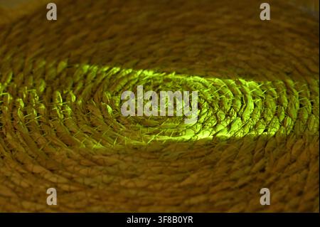 Commercial close-up macro photograph of an abstract vibrant green light beam or laser slicing across the complex, swirling texture of a circular woven straw mat or coaster against a dark background. Stock Photo