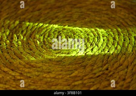 Commercial close-up macro photograph of an abstract vibrant green light beam or laser slicing across the complex, swirling texture of a circular woven straw mat or coaster against a dark background. Stock Photo