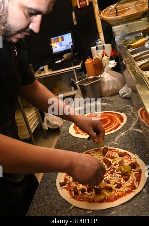 Chef in restaurant preparing and adding items on pizza Stock Photo