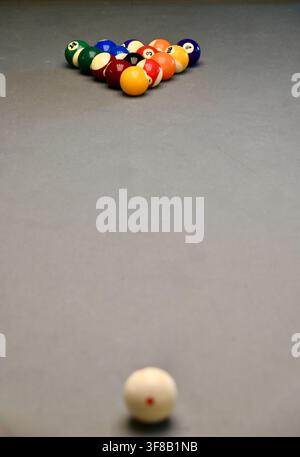 Commercial top-down photograph of a racked set of colorful billiard balls and a cue ball positioned on a sleek gray pool table, ready for a game. Stock Photo